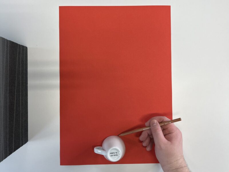 Bild, das zeigt wie mit einer Espresso-Tasse ein Kreis auf rotem Zeichenpapier eingezeichnet wird.