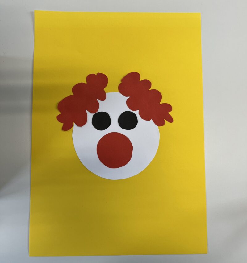 Das Bild zeigt die auf einem gelben Papier aufgeklebten Einzelteile, welche zusammen die Form eines Clowns ergeben